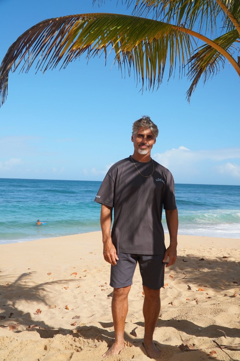 Man standing on a beach with palm leaves and ocean in the background